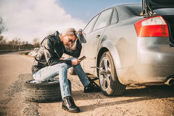 extended car warranty woman sitting on tire with phone in hand car breakdown open trunk USAA 